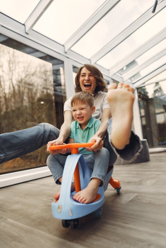 A joyful moment of a mother and son playing indoors on a toy car, showcasing love and happiness.