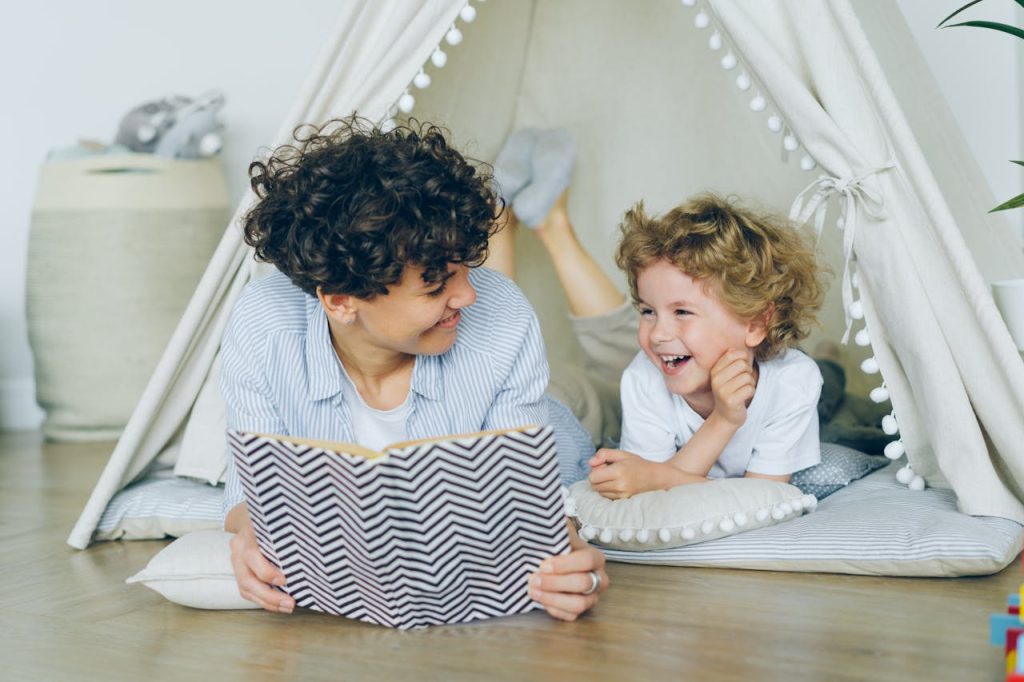 A joyful mother and son enjoying reading together in a cozy indoor tent setting.